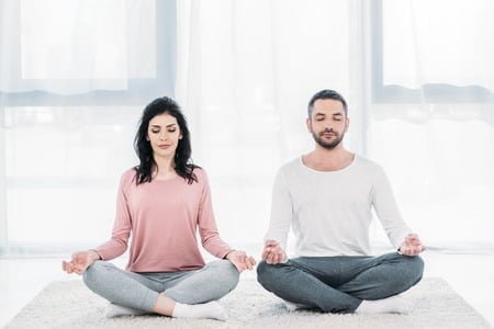 121966382 woman and man with eyes closed sitting in lotus pose and meditating at home