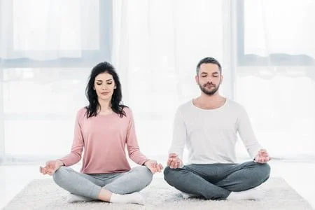 121966382 woman and man with eyes closed sitting in lotus pose and meditating at home